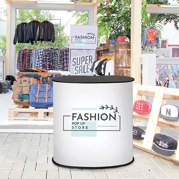 Messedisk med "Fashion Pop Up Store" logo og tøjudstilling i baggrunden