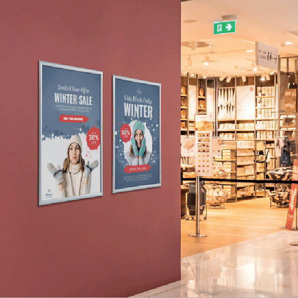 To aluminiumssnaprammer med vinterplakater hænger på en rød væg i butik.