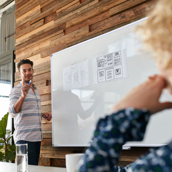 Mand underviser ved whiteboard med wireframes og tilhørere på kontor.